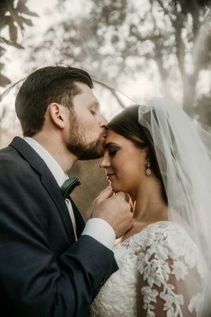 Romantic outdoor wedding portrait showing gentle intimacy between newlyweds with soft forest lighting.
