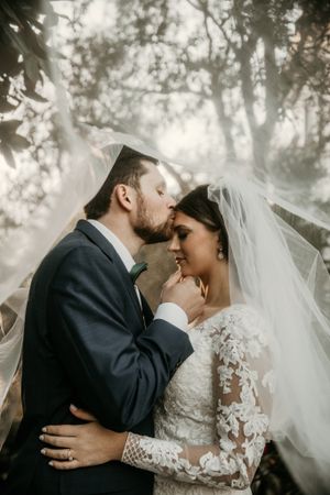 Artistic wedding portrait showing tender embrace between newlyweds with dreamy forest backdrop.