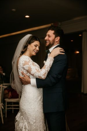 A bride in lace sleeves and groom in dark suit share an intimate moment during their first dance at a wedding reception.