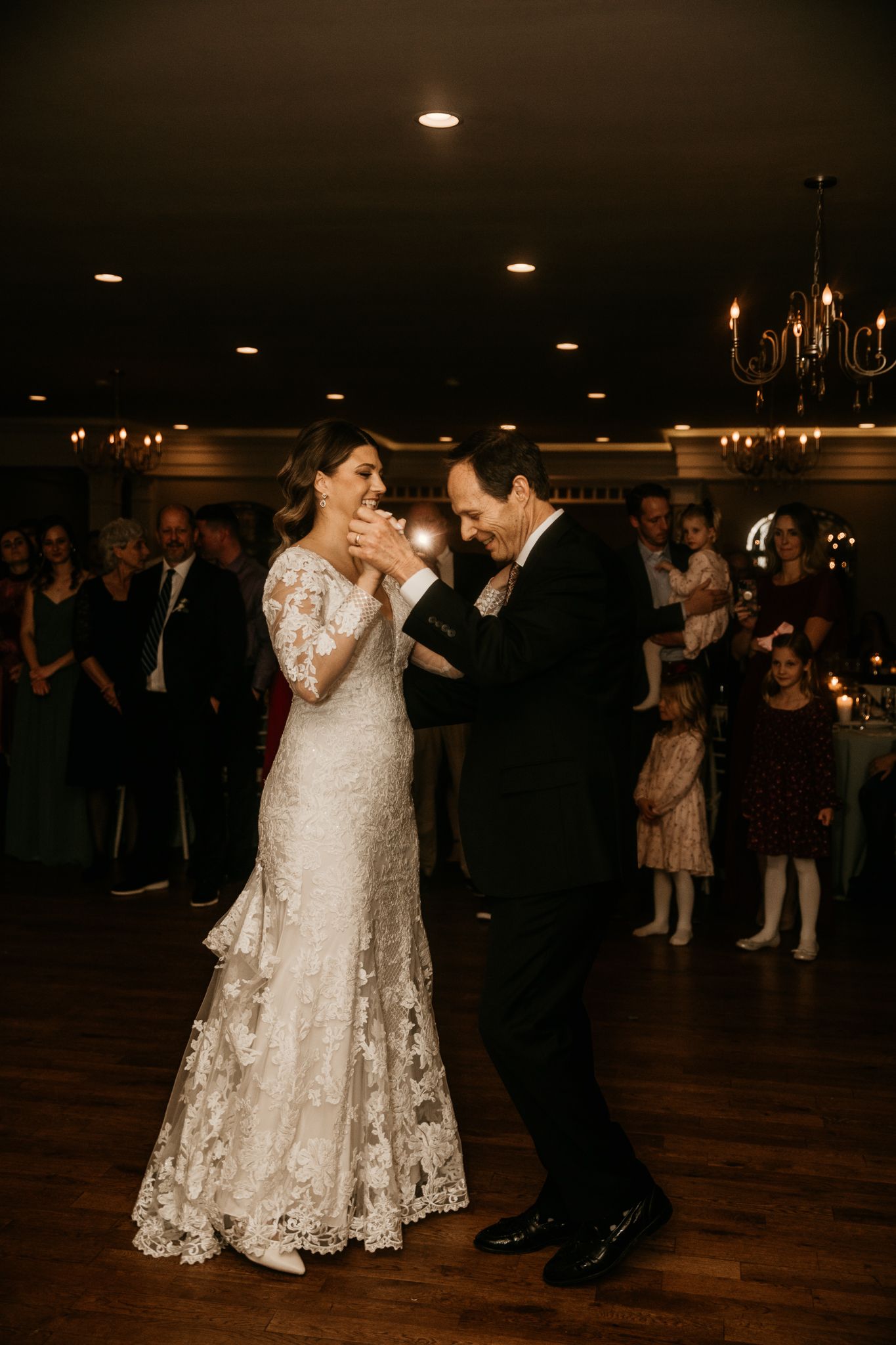 A couple shares a joyful dance moment on their wedding day in a dimly lit reception venue.