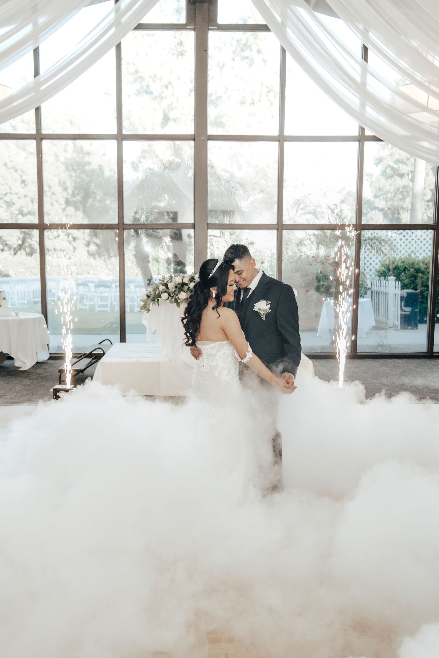 Newlyweds dancing in fog effects inside a chapel with dramatic window lighting.