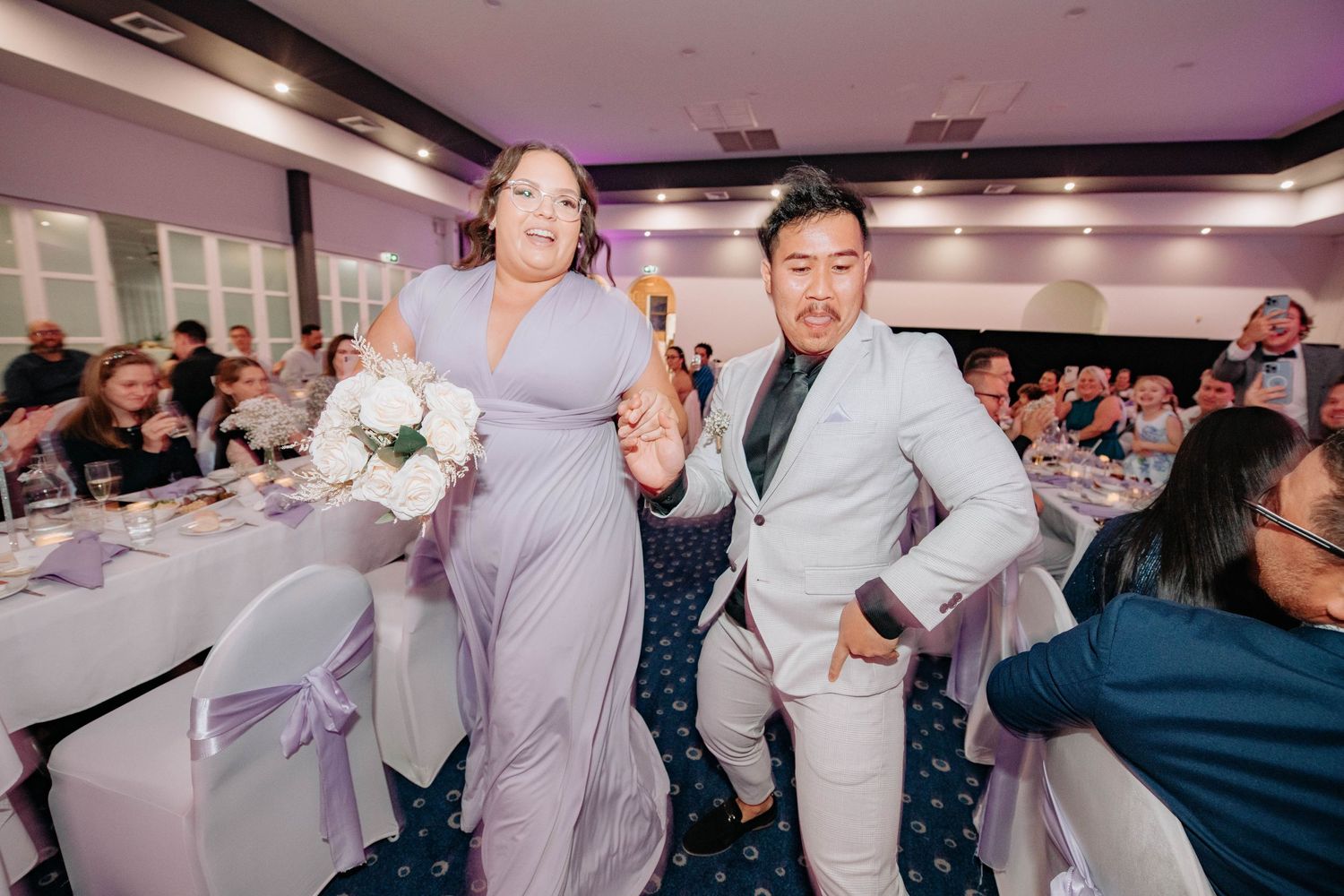 Wedding party members in light colored attire dance together during the reception celebration.
