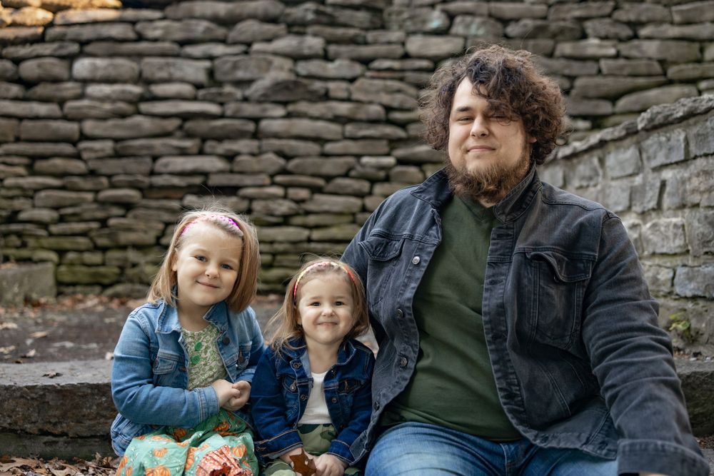 A casual outdoor family portrait against a stone wall.