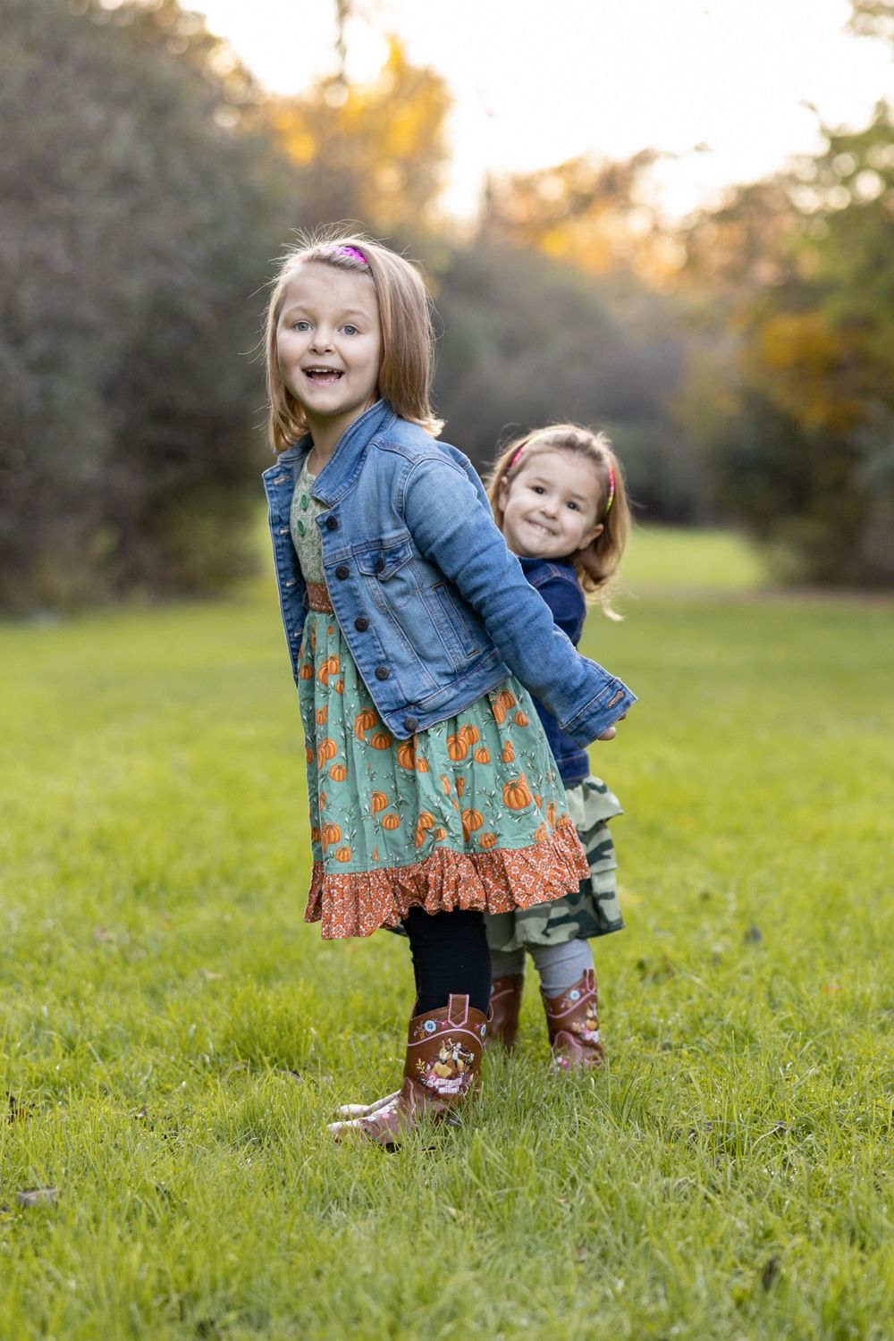 Two children playing and laughing together in a grassy field at sunset.