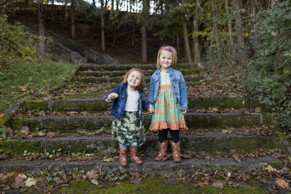 Two children stand together on moss-covered stone steps in an autumn forest setting.