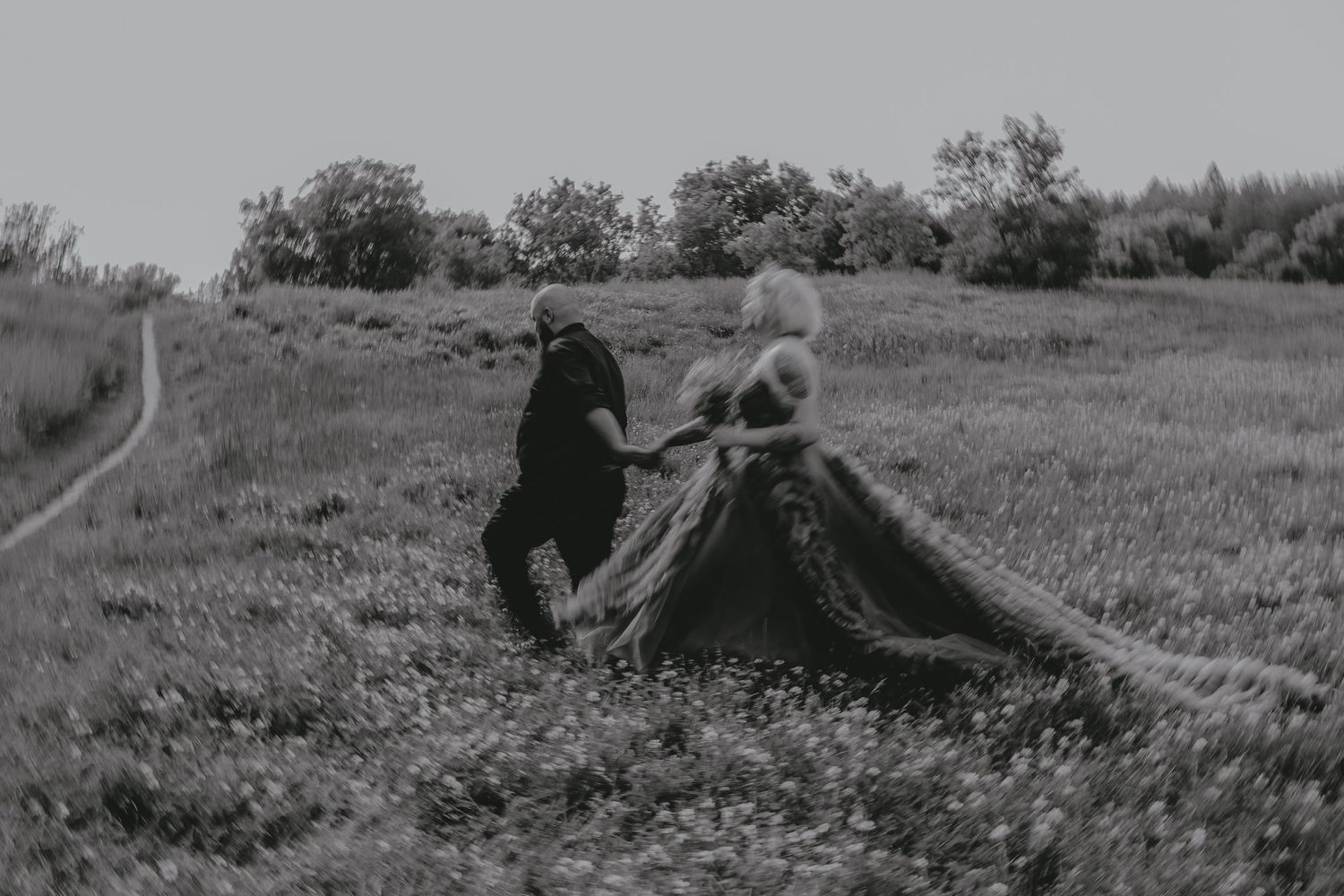 A recently eloped couple walk through a field.  The bride is wearing an elaborate dress.