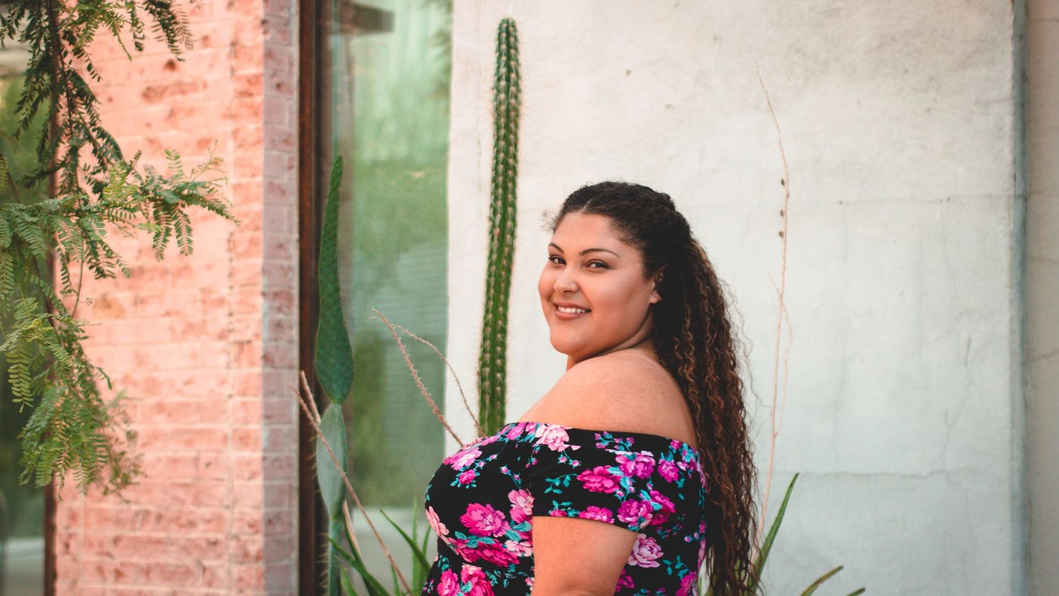 Outdoor portrait session against rustic brick wall with potted plants.