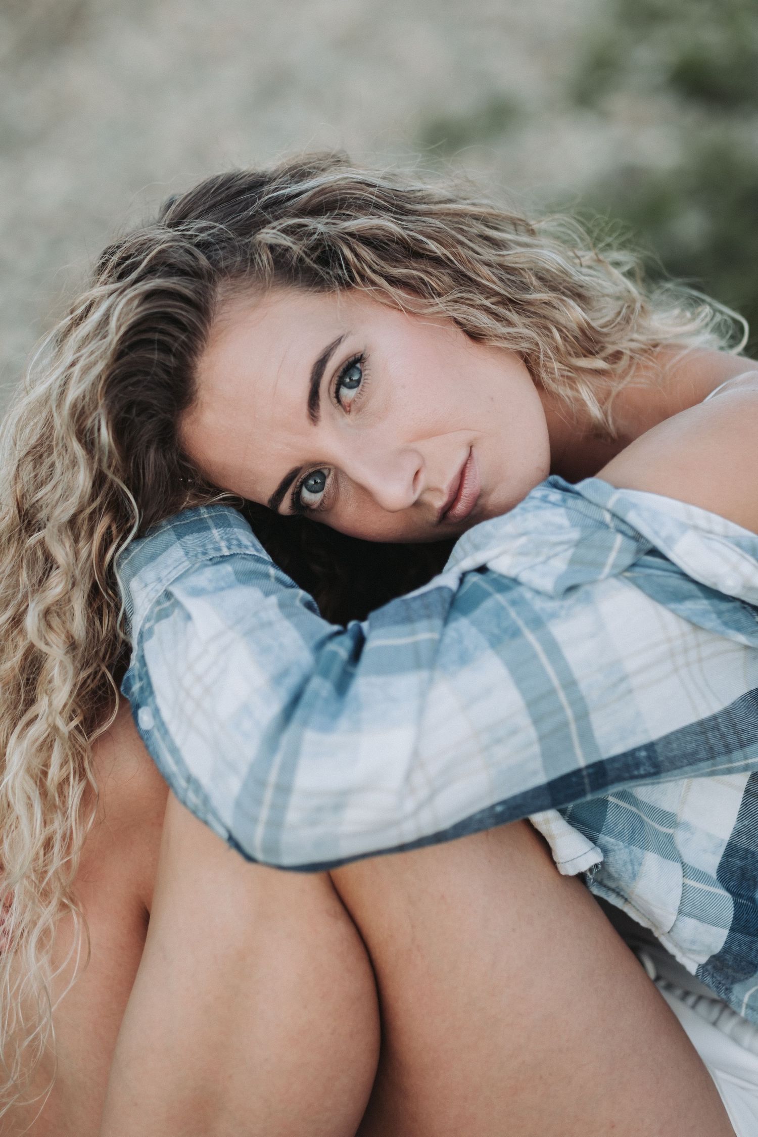 Close up portrait of person with curly hair in plaid shirt resting on knees.