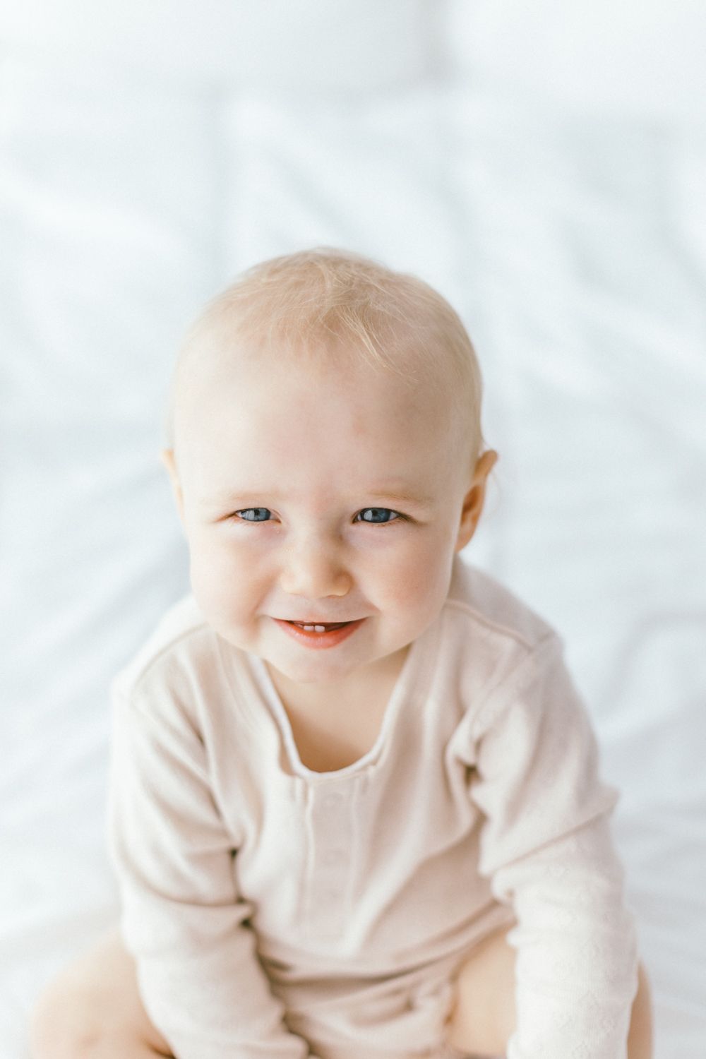 Smiling baby wearing light beige sweater against white background.