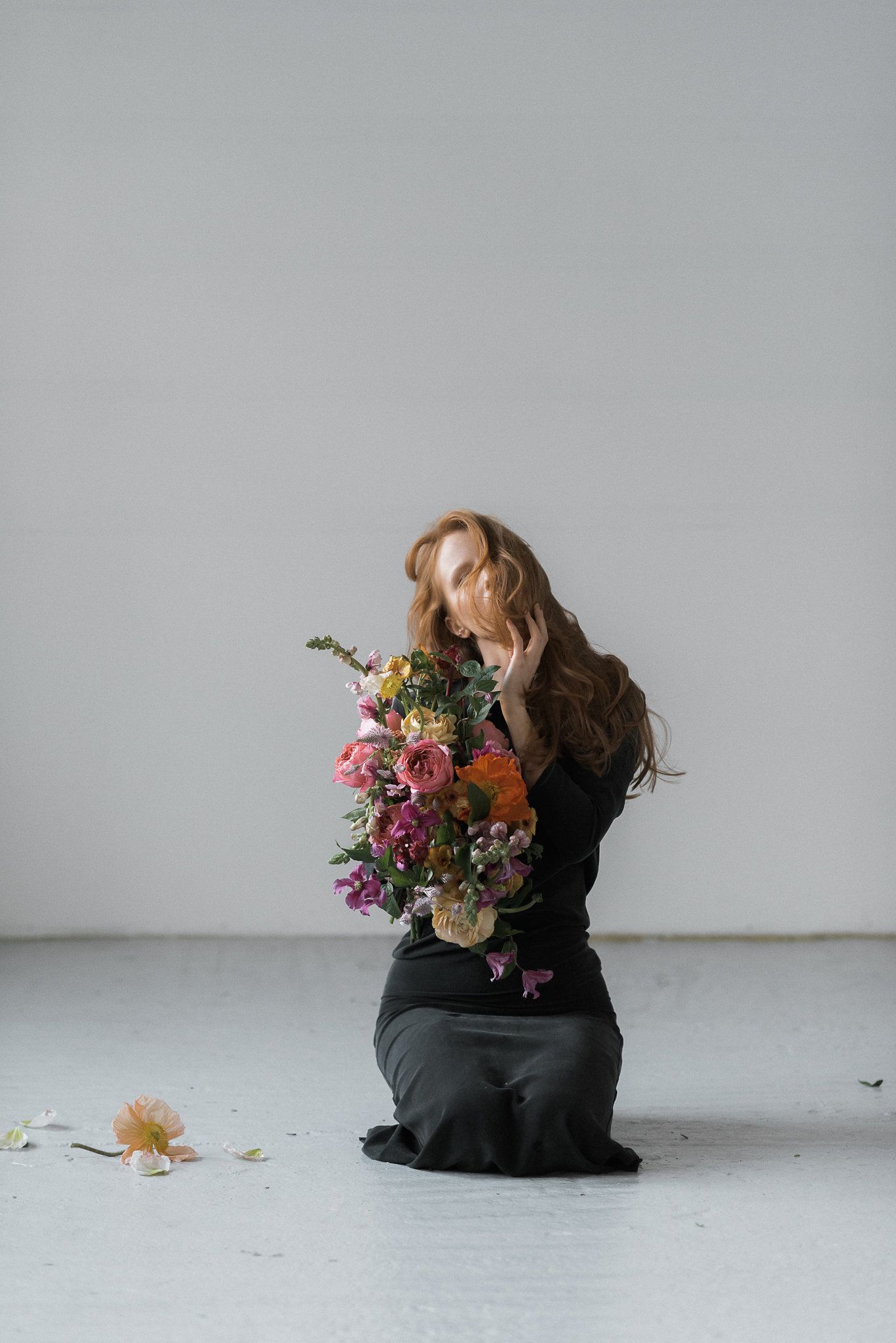Woman in black holding vibrant floral bouquet against white studio backdrop.
