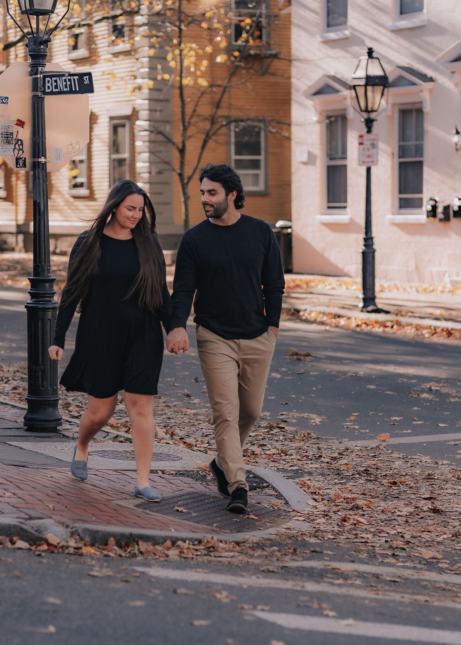 A couple walks together on a cobblestone street (Benefit Street in Providence) with autumn leaves and vintage lampposts on a fall afternoon.
