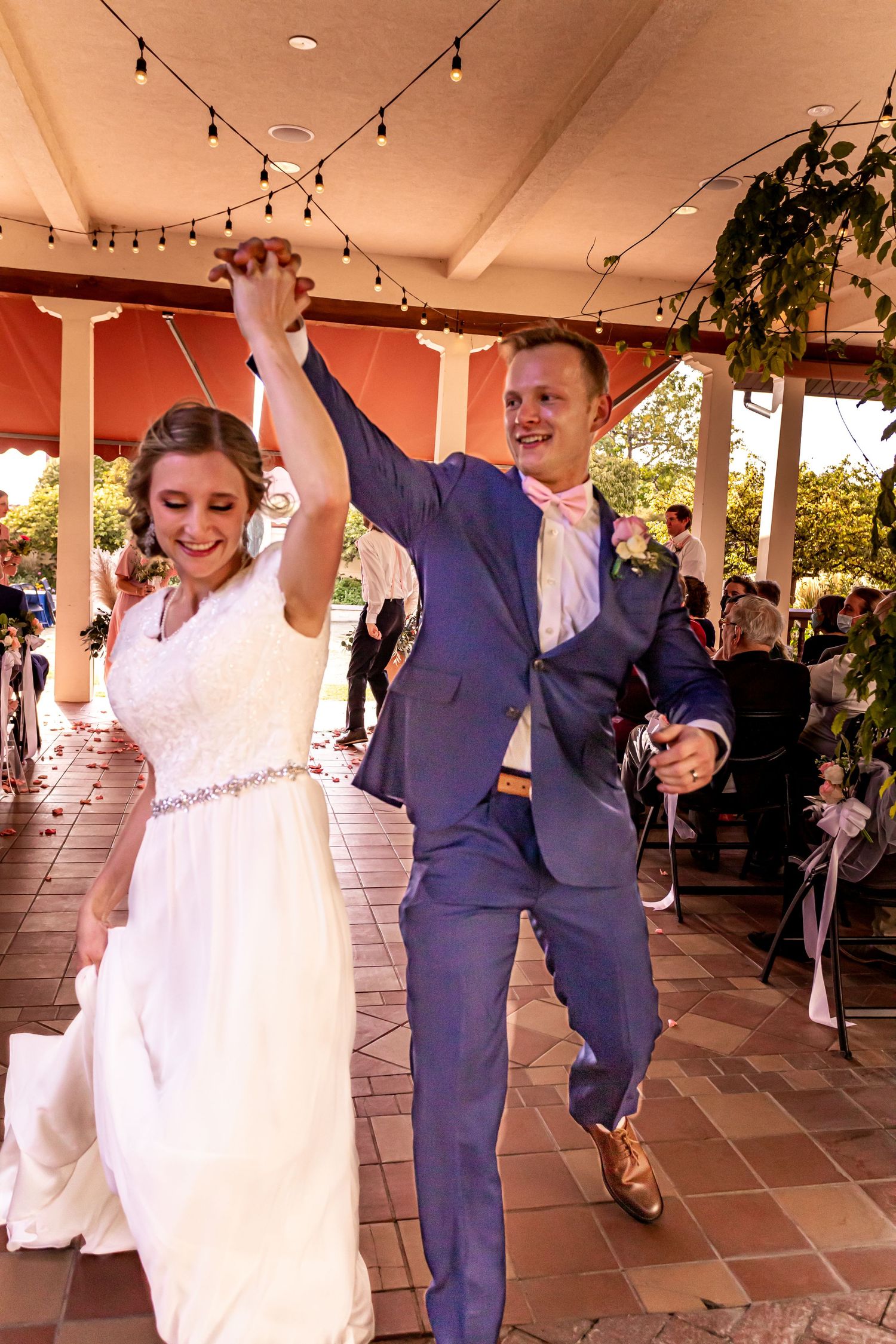 Newlyweds celebrate with a joyful dance under string lights at their outdoor reception.