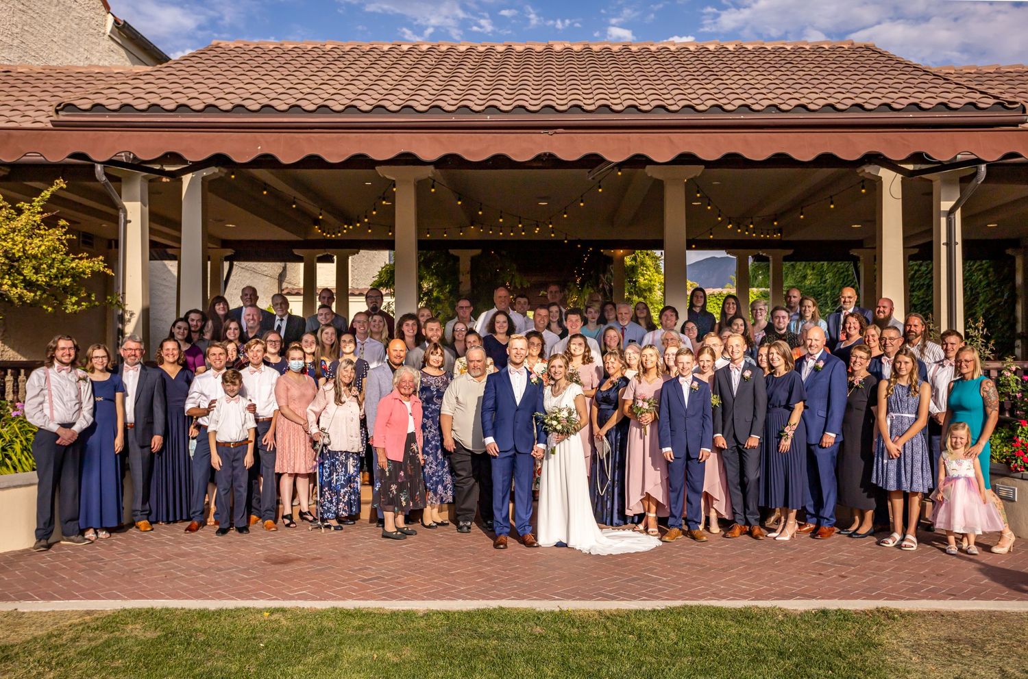 Large wedding group photo of guests and wedding party gathered under a Spanish-style covered patio.