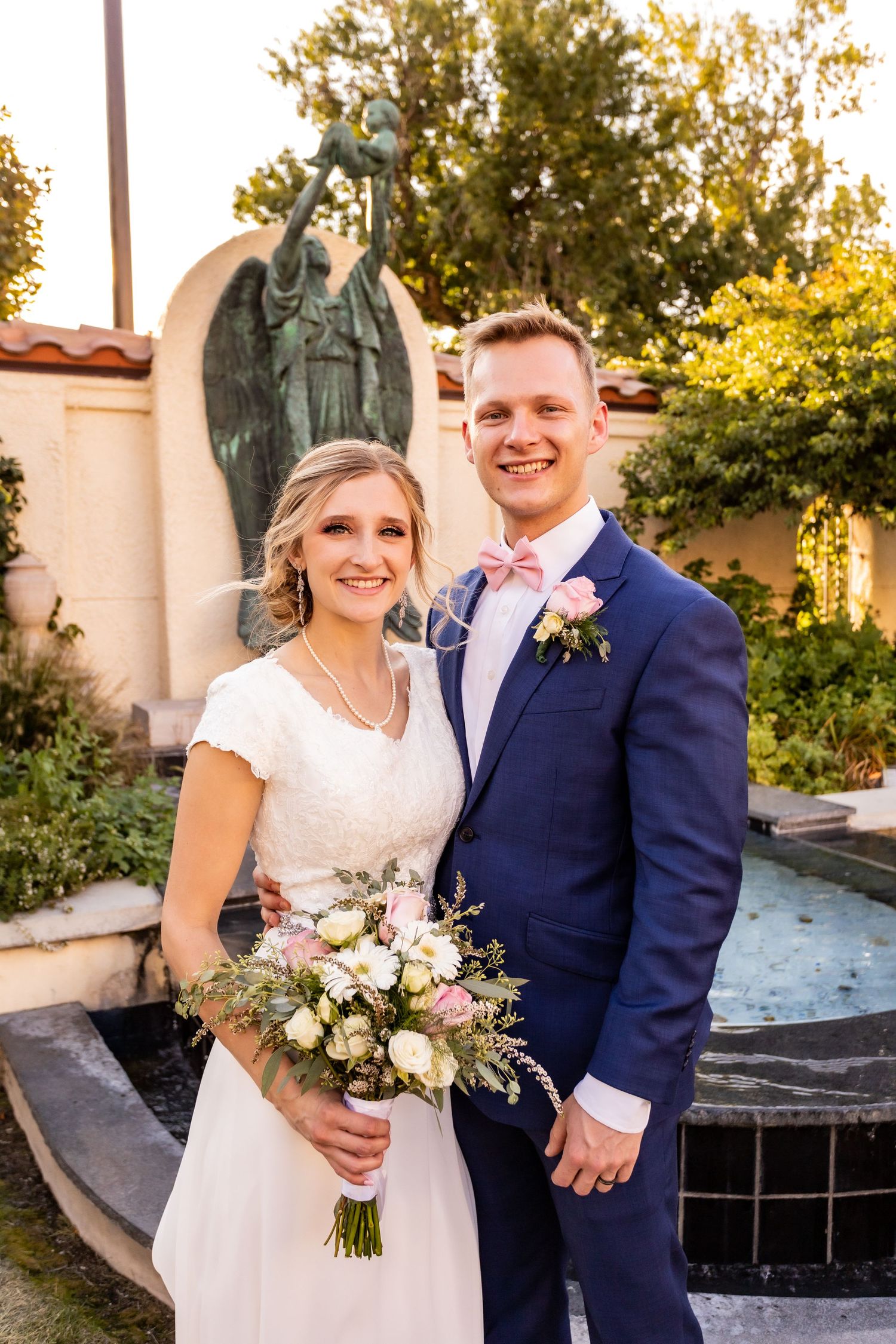 Wedding portrait in front of stone angel statue and garden setting.