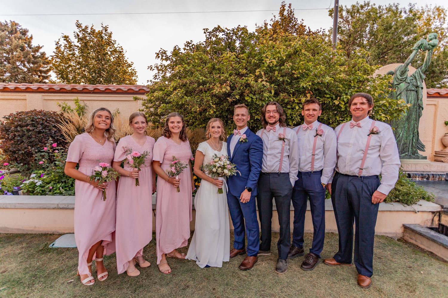Wedding party photo with bridesmaids in pink dresses and groomsmen in blue suits.