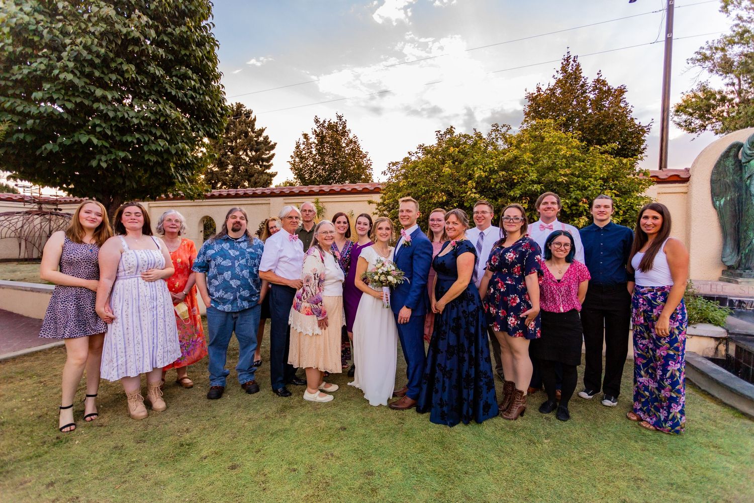 Wedding party group photo with guests in blue and pink attire outdoors.