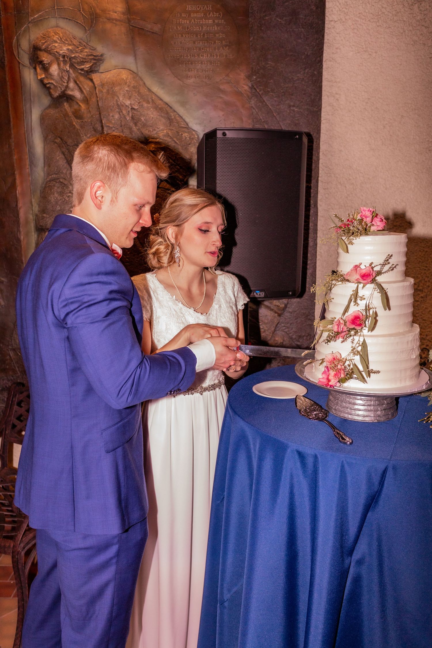 Elegant white wedding cake with pink floral decorations being cut at a reception.