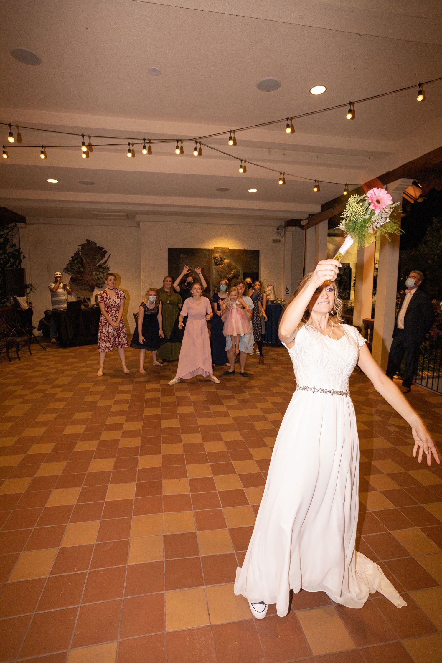 Wedding reception dance with flowing white dress and string lights on terracotta tile floor.