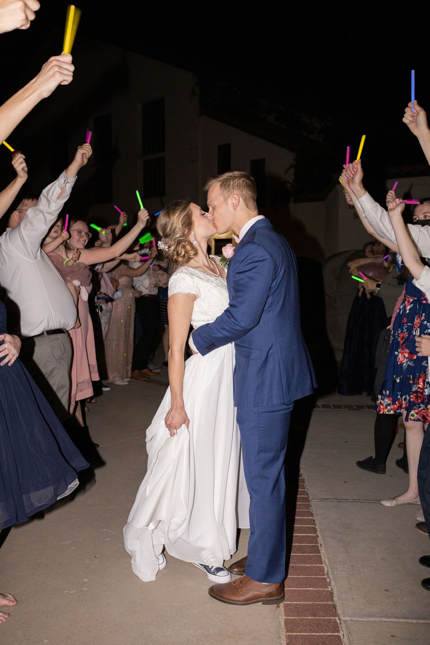 Wedding exit with guests holding colorful glow sticks during nighttime celebration.