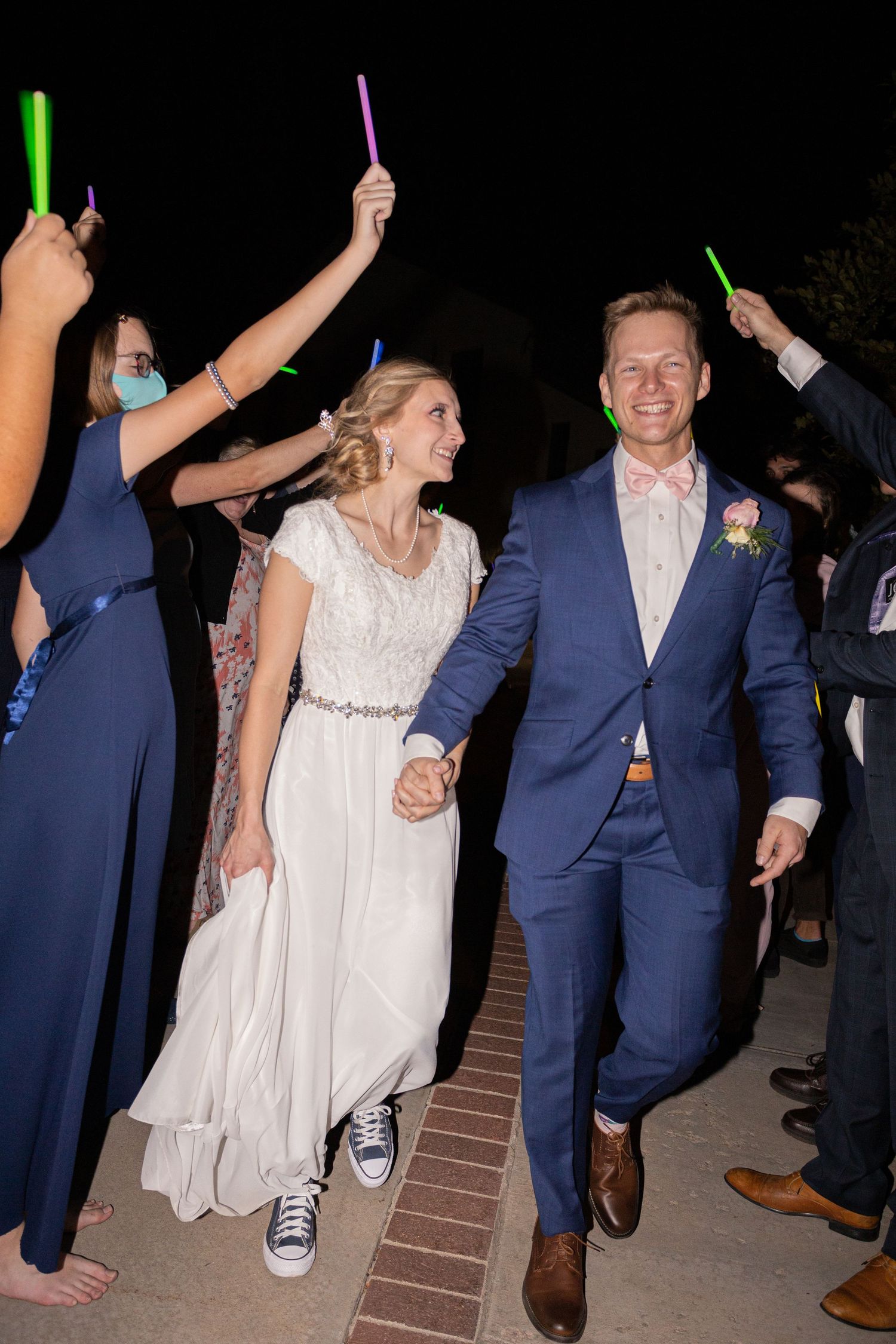 Wedding couple exits through tunnel of glow sticks held by guests at night.
