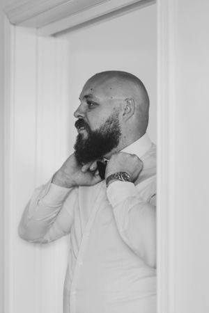 Black and white portrait of a bearded man adjusting his collar in formal attire.