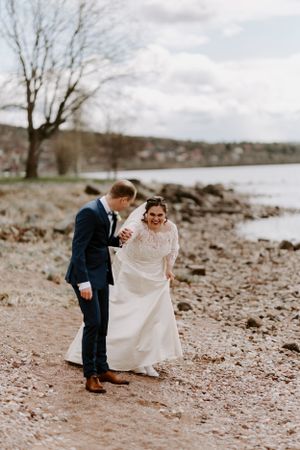 A couple shares a joyful moment together on a rocky beach shore during their wedding photoshoot.
