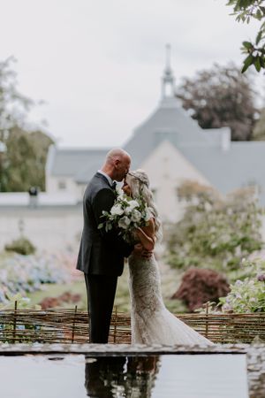 Romantic wedding couple embraces near church with white floral bouquet.