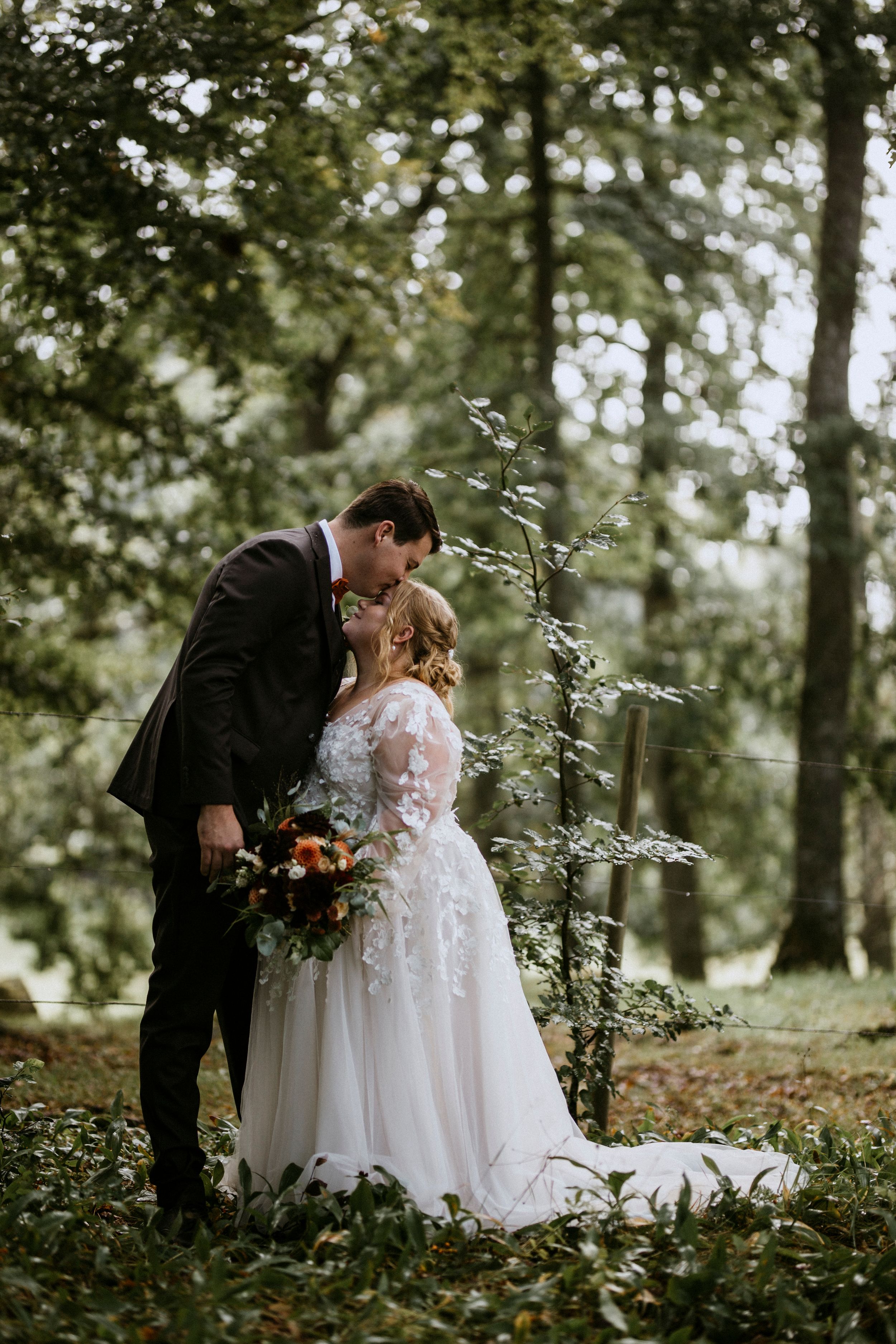 Intimate wedding moment captured in a wooded setting with fall foliage.
