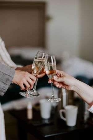 Two people clink champagne glasses together in a toast during an intimate indoor celebration.