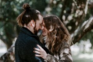A couple shares an intimate moment together against a blurred natural background.