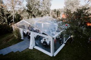Clear tent wedding reception venue setup with white draping in garden setting.