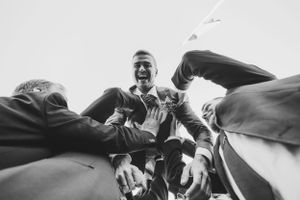 Black and white photo of groomsmen lifting someone in celebratory pose.