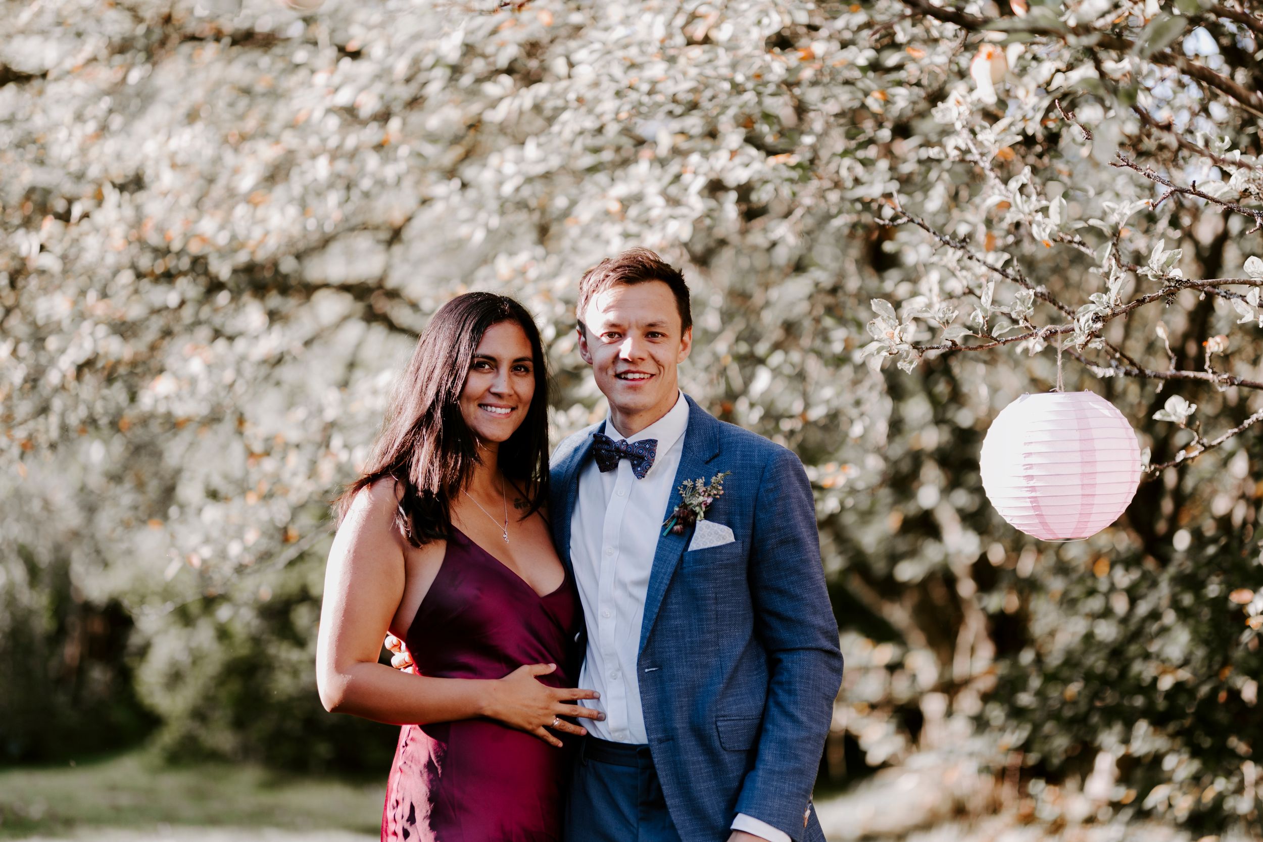 Couple poses together during spring celebration with cherry blossoms and pink lantern.