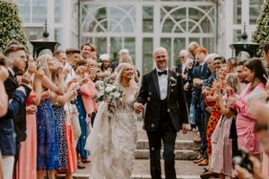 Wedding exit with guests cheering and clapping in formal garden setting.