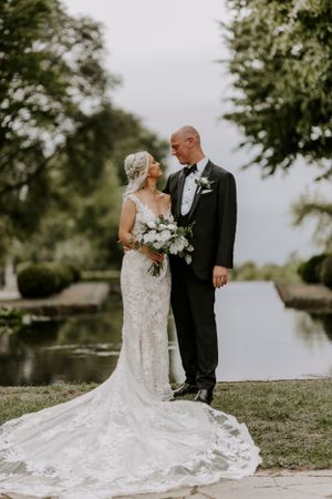 A romantic wedding portrait of a couple by a reflective pond surrounded by trees.