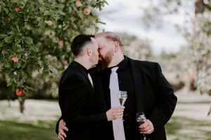 A couple shares a romantic moment while holding champagne glasses in an apple orchard.