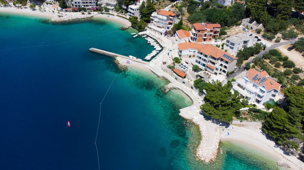 Aerial view of a coastal village with white buildings and turquoise waters in a Croatian bay.