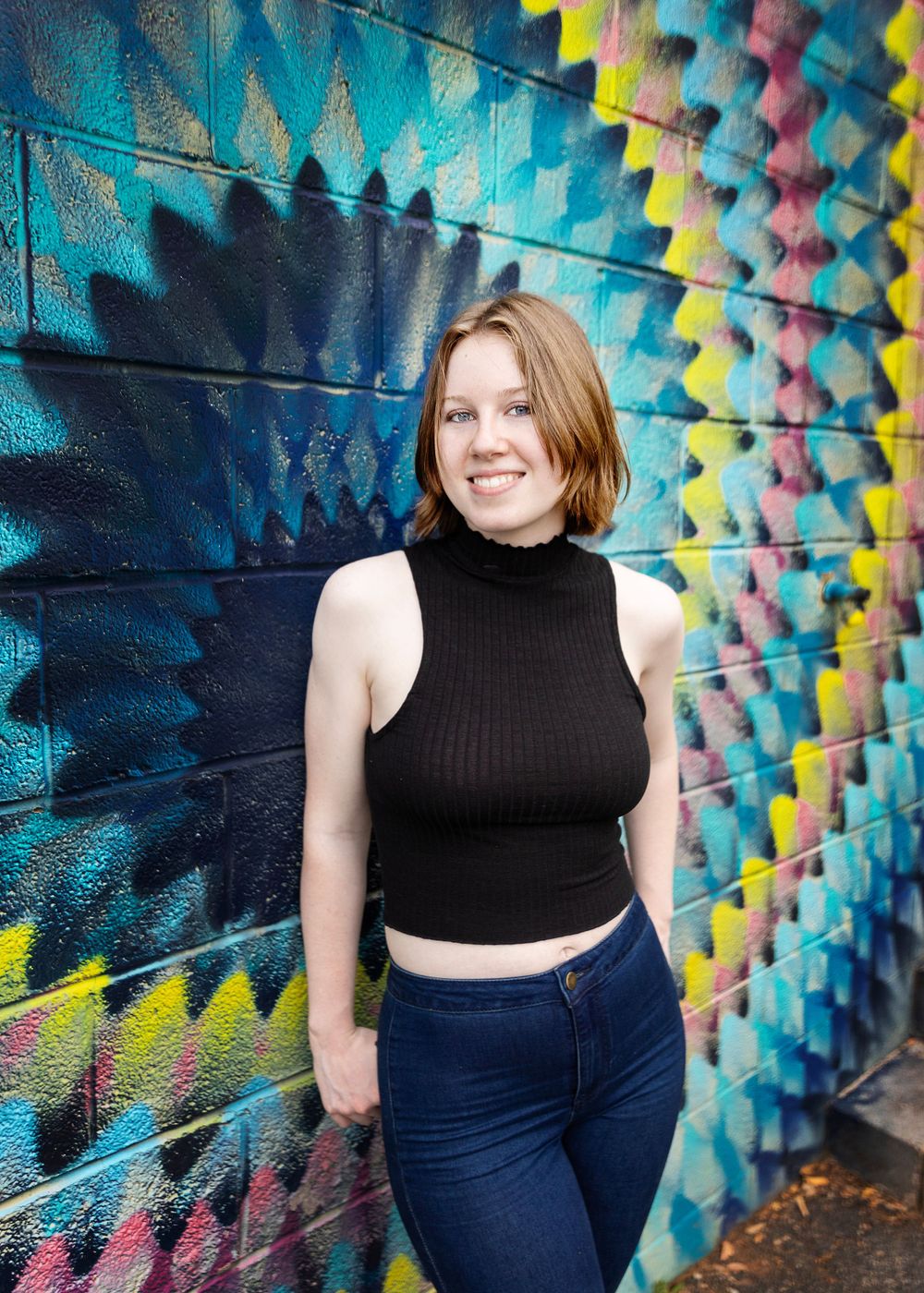 Person in black crop top poses against vibrant geometric street art mural.