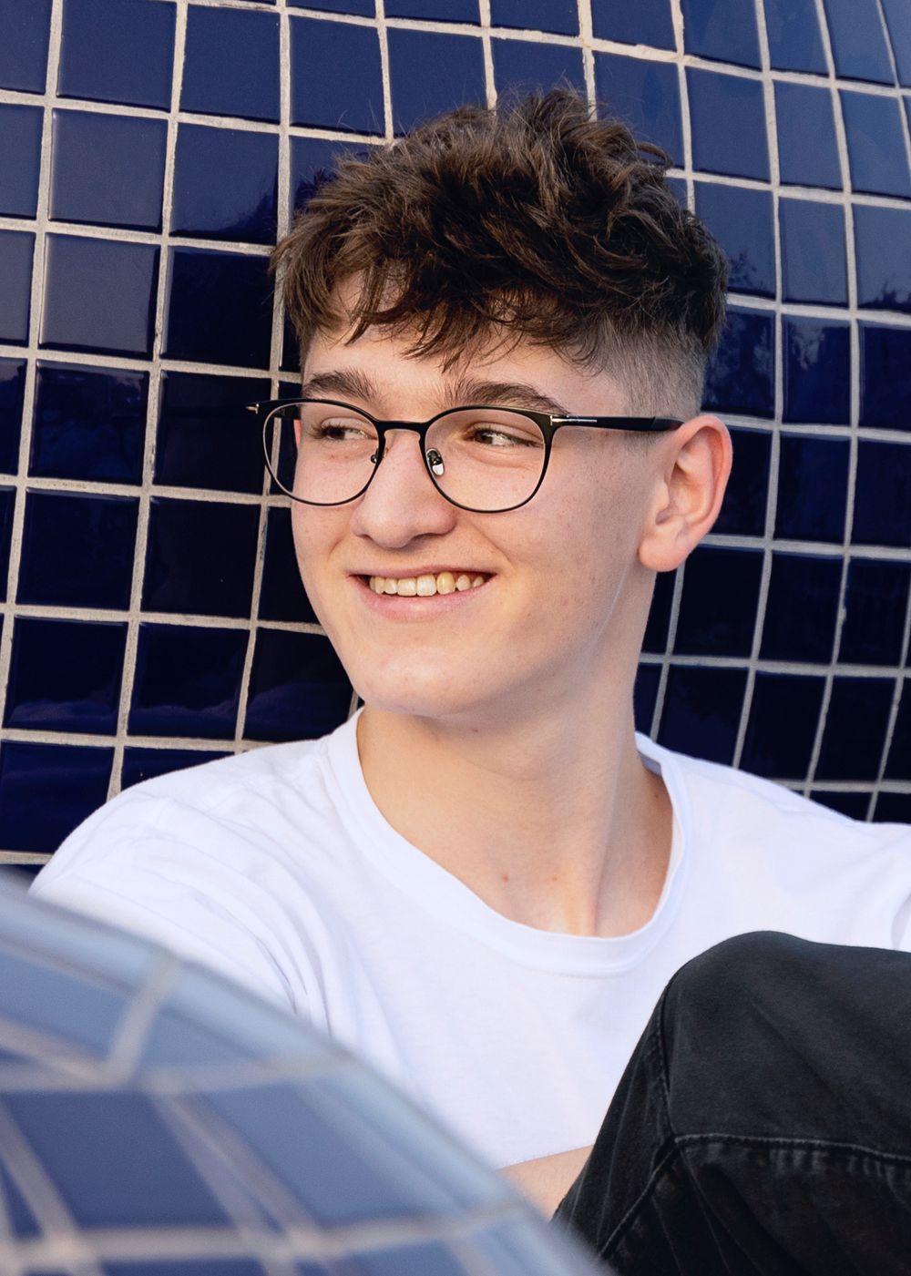 Close up of senior boy posing around blue tile outdoor structures during a senior portrait session.