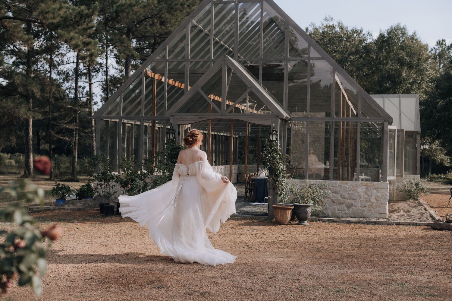 White wedding dress twirling in front of a modern greenhouse structure.