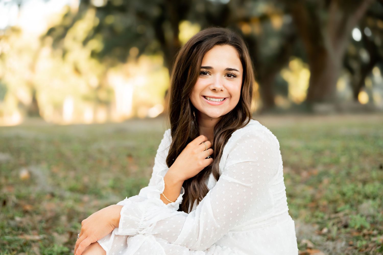 Elegant outdoor portraits in a white dress with natural lighting and trees in background.