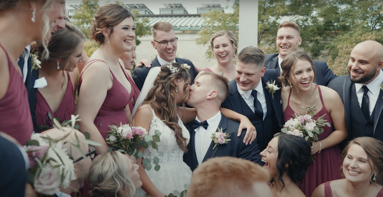 Wedding party shares laughter during a group photo outside.