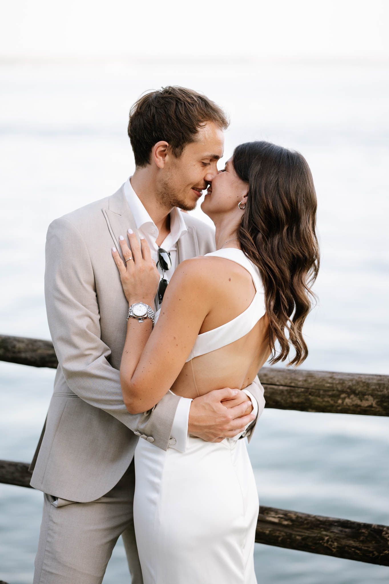A romantic seaside moment between newlyweds in formal attire against an ocean backdrop.