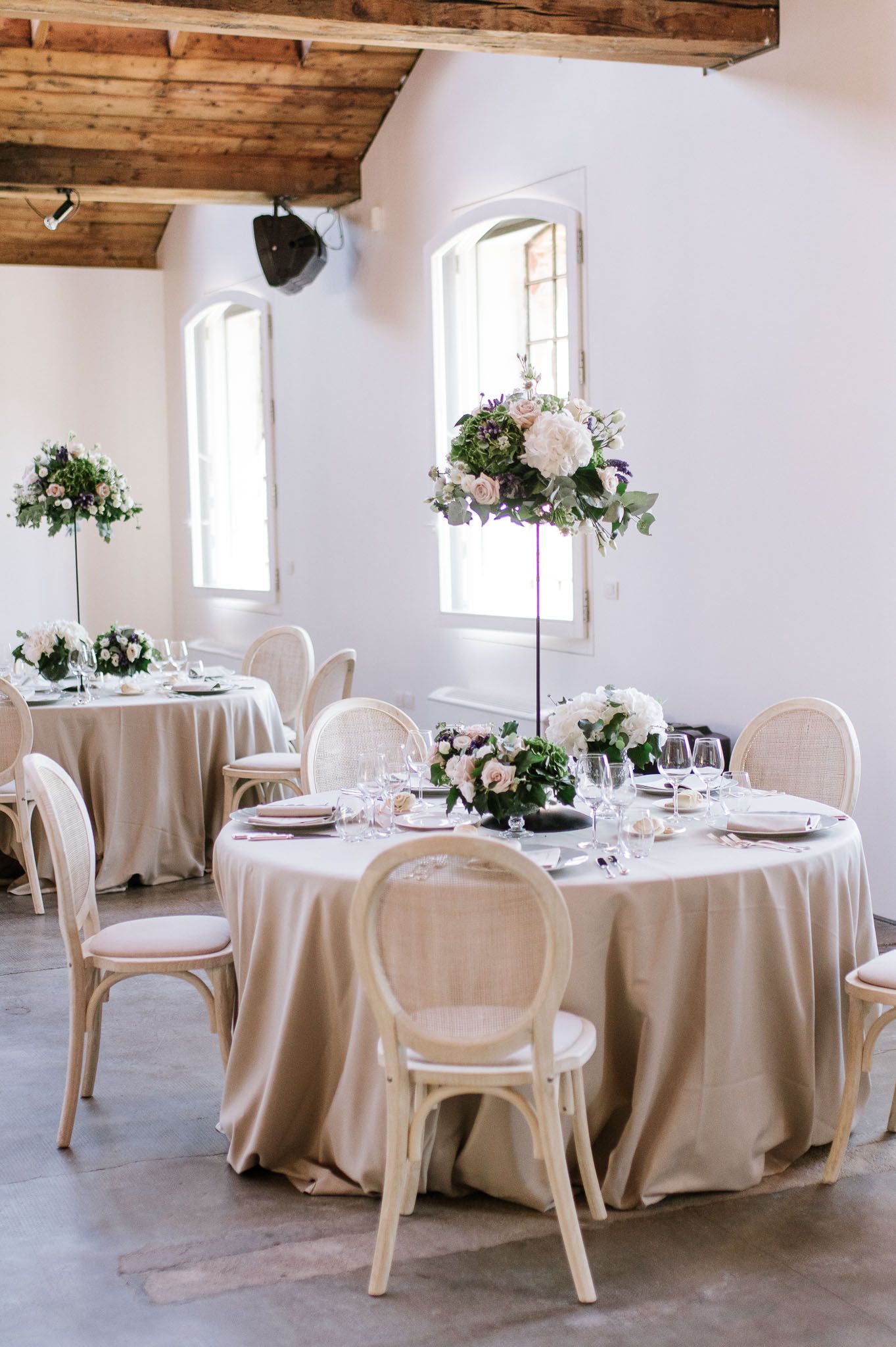 Elegant wedding reception setup with round tables, cream linens and floral centerpieces.