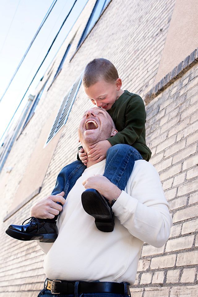 A joyful moment between parent and child with the child sitting on shoulders against a brick wall.