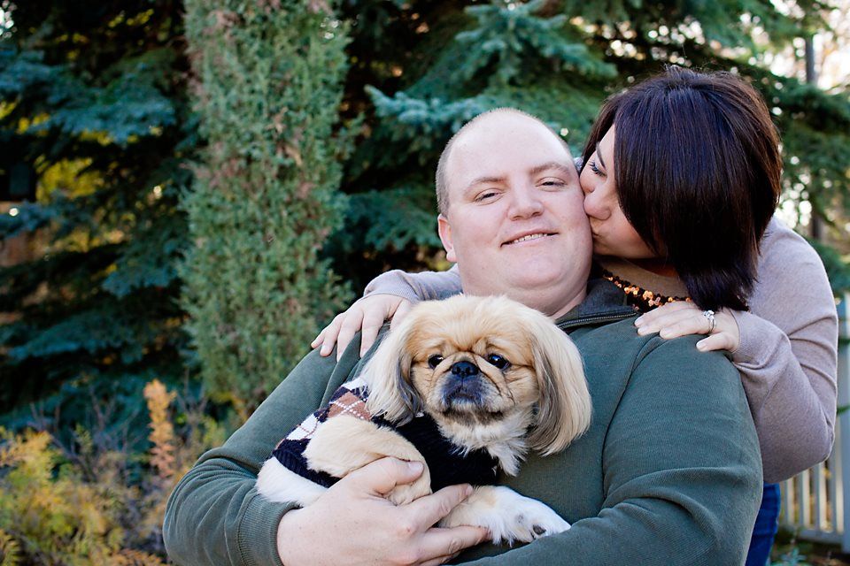 A couple snuggling with their small Pekingese dog outdoors on an autumn day.