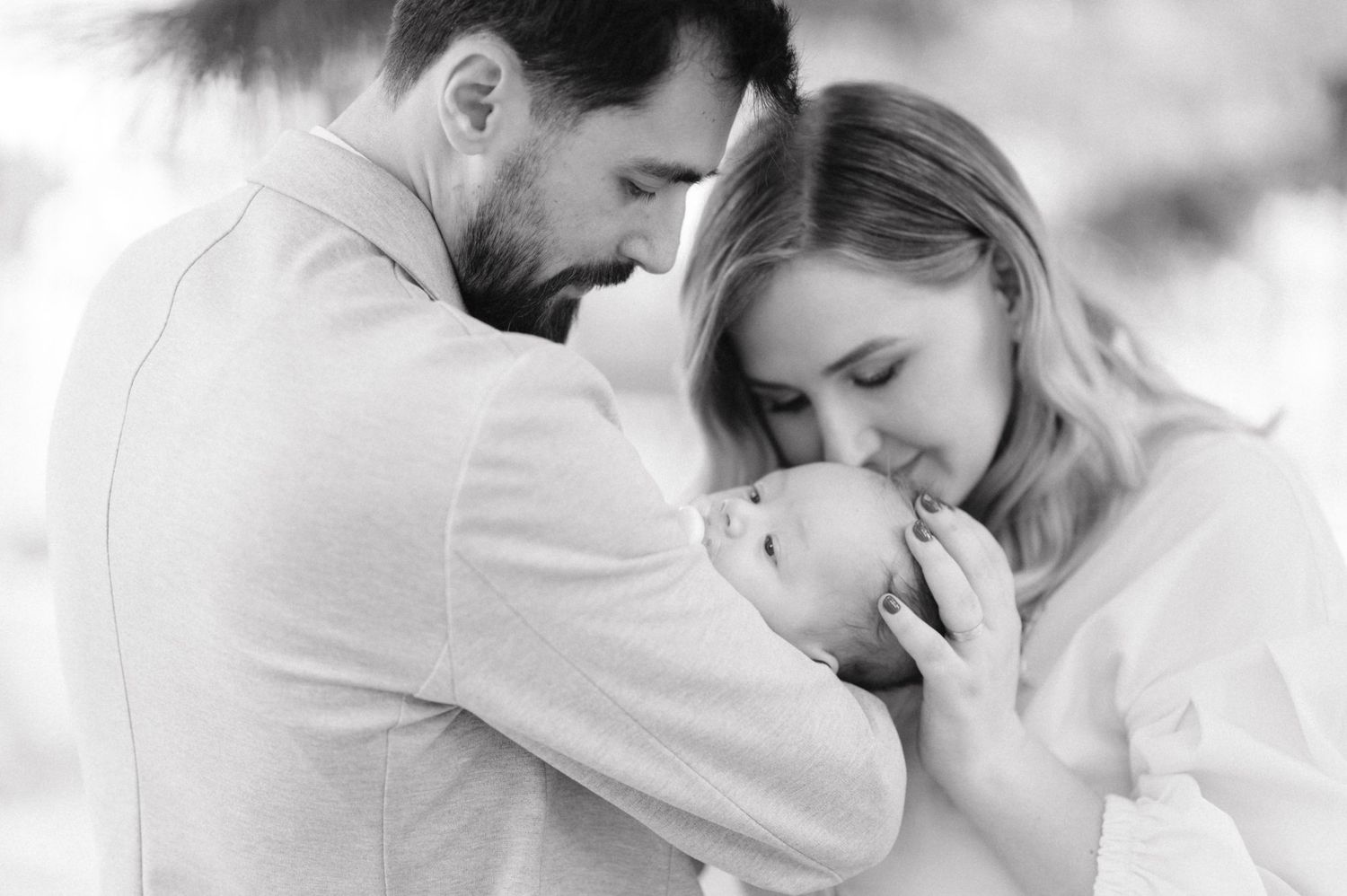A tender family moment with parents embracing their newborn baby in black and white.