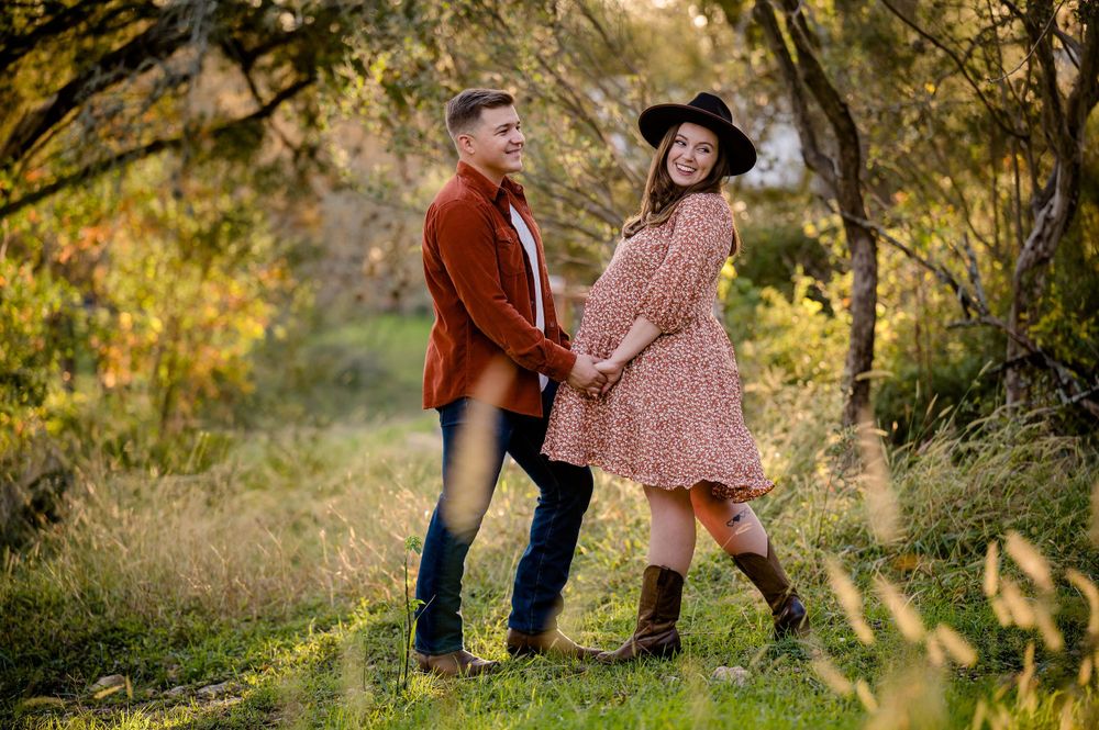 Playful maternity portrait of couple in coordinating outfits against autumn foliage.