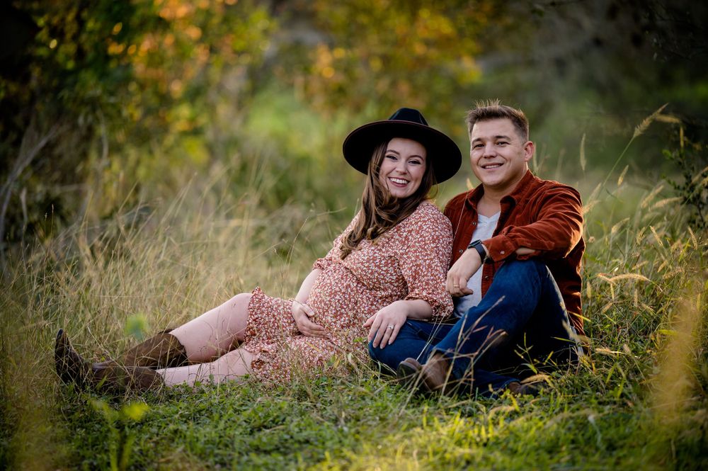 Couple relaxes together on grassy hillside during outdoor maternity session.