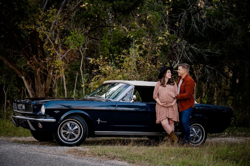 Expecting couple poses with classic blue Mustang car during outdoor photo session.